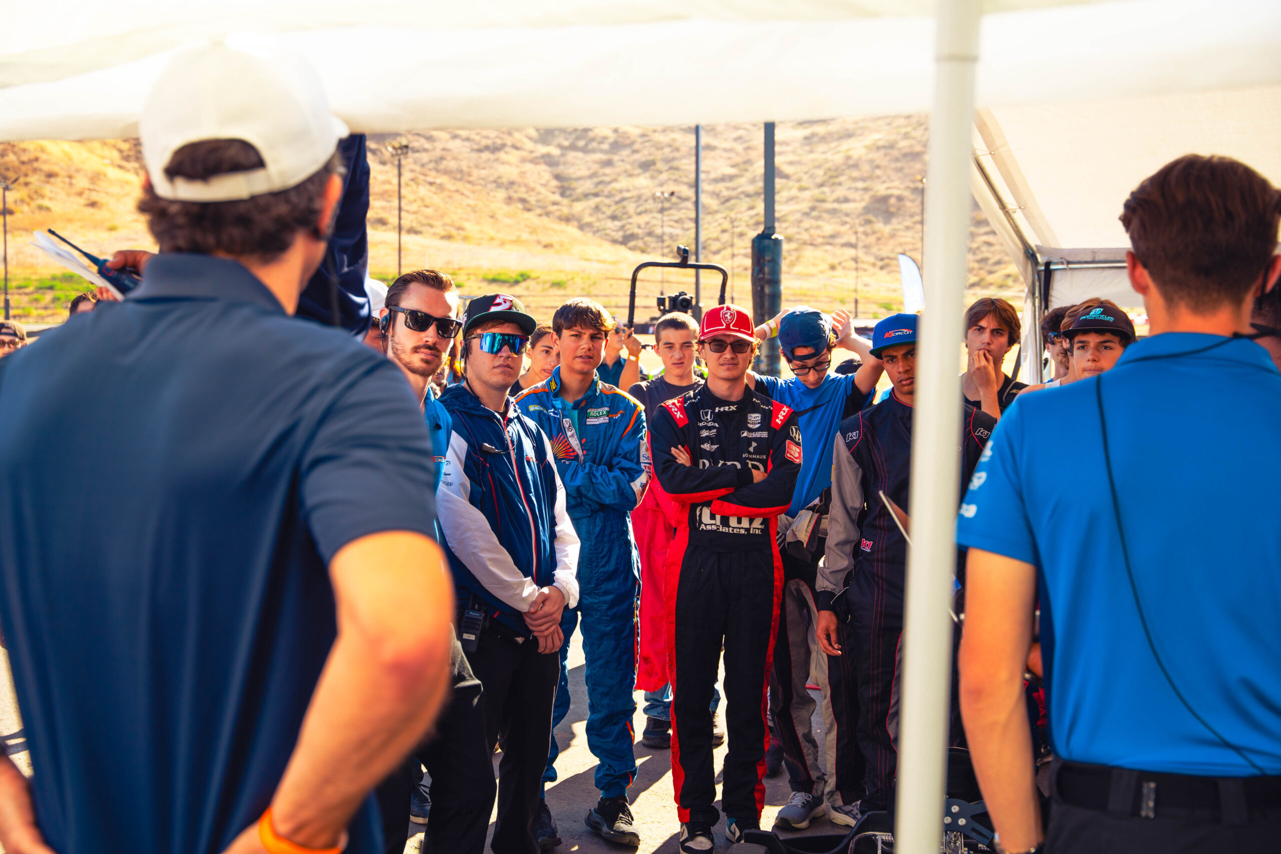 a crowd of racers listen to someone speaking at k1 circuit